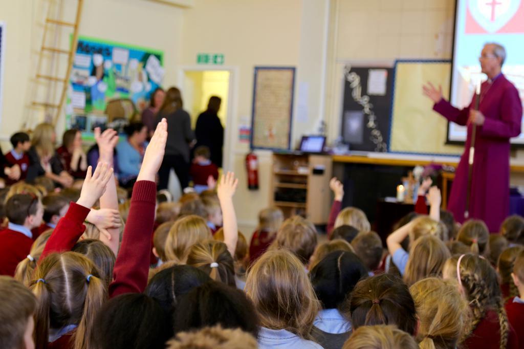 Children with hands up in assembly